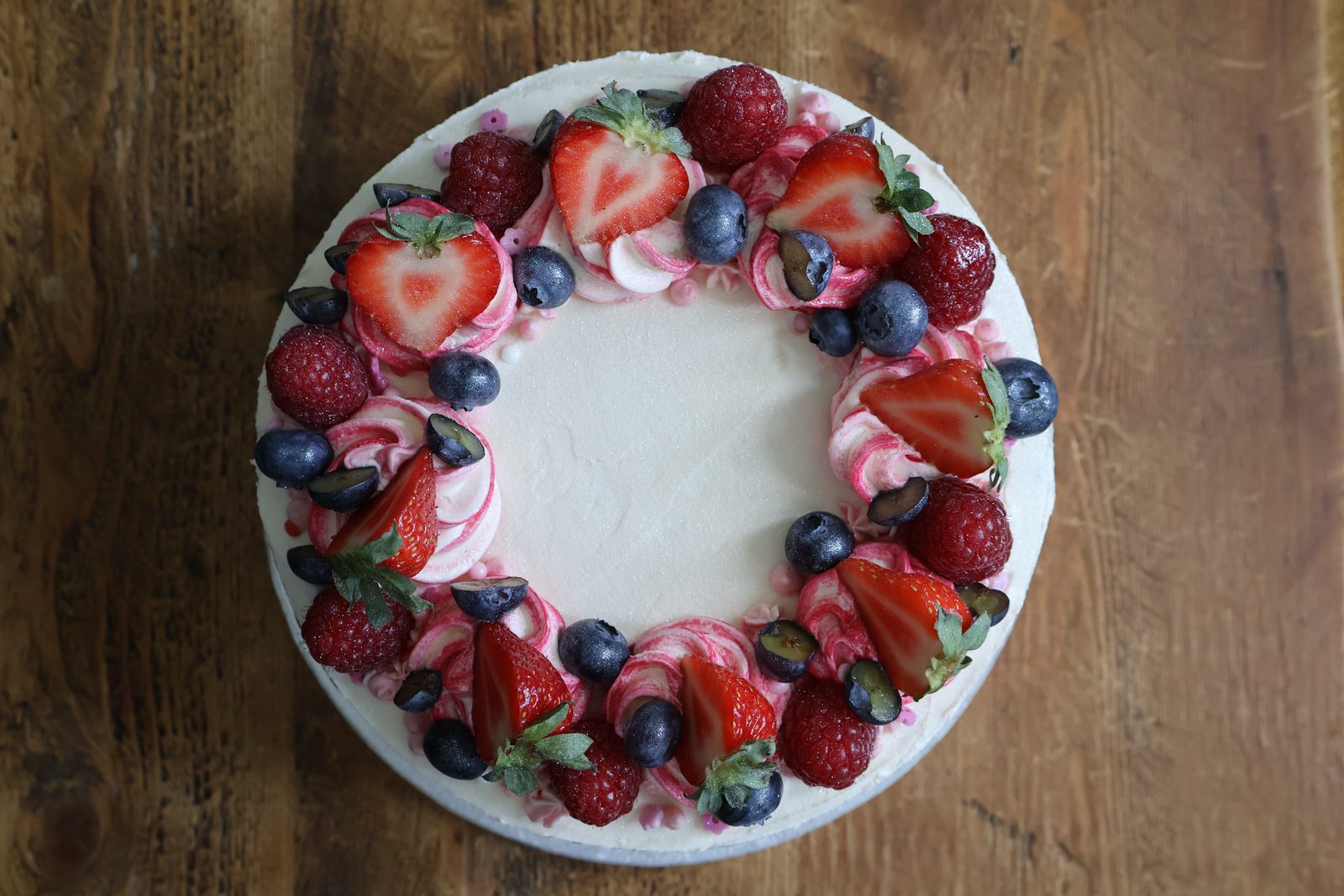 Overhead view of a cake topped with a ring of strawberries, raspberries, blueberries and pink piped buttercream
