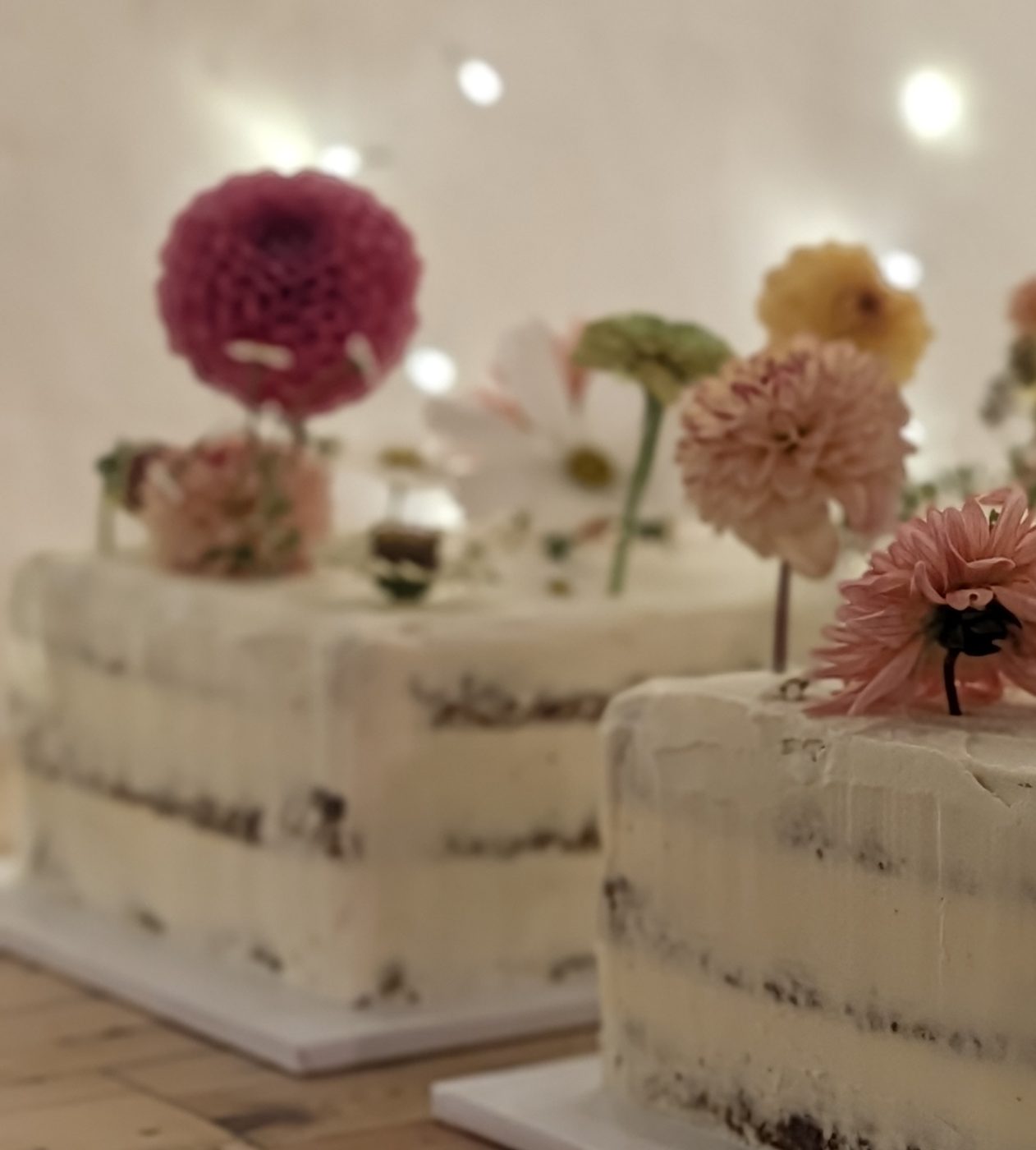 Two semi-naked sponge cakes topped with fresh dahlias and cosmos flowers