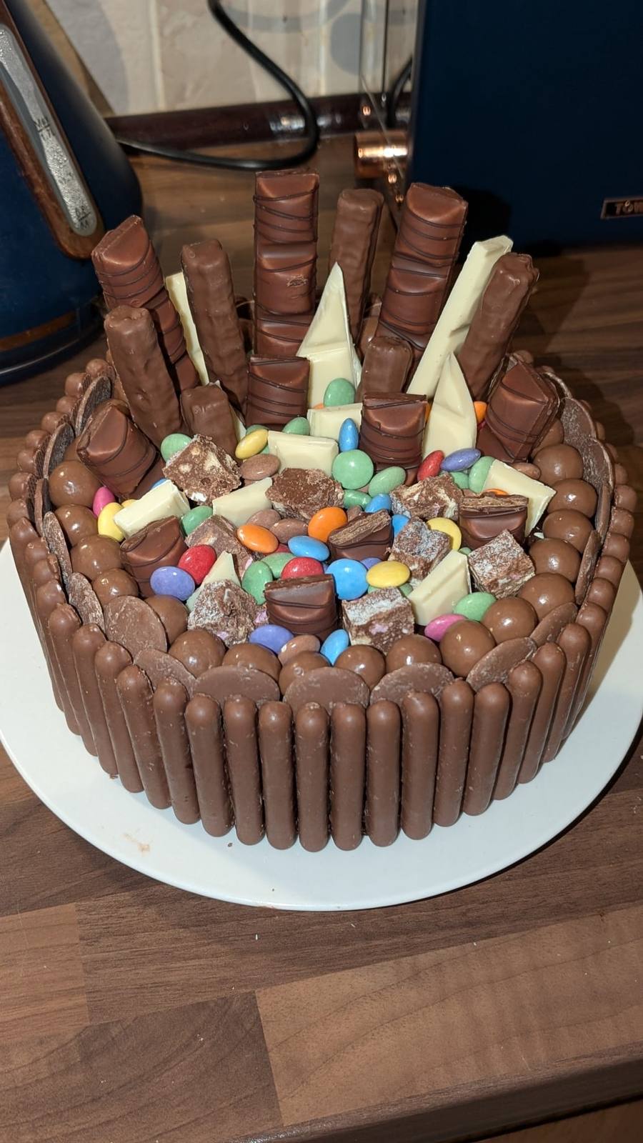 Chocolate cake covered in chocolate fingers, sweets and white chocolate shards